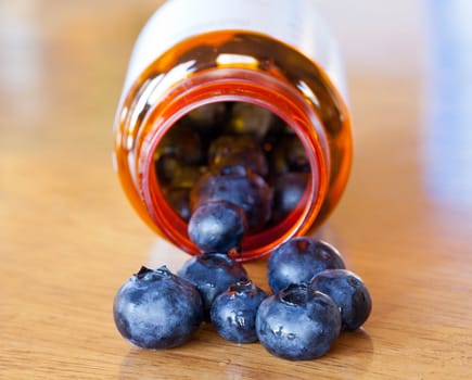 Fresh blueberries being poured from orange prescription bottle onto wooden table for breakfast