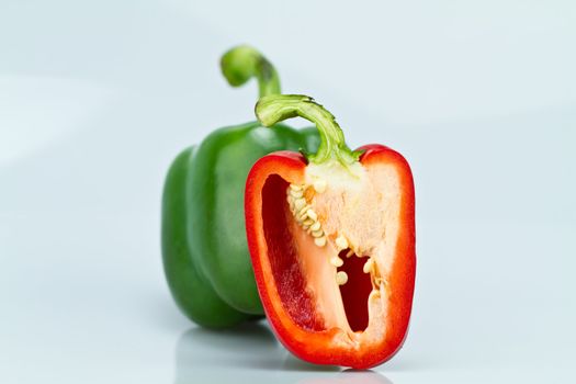 The green whole capsicum and cut red capsicum on bluish background