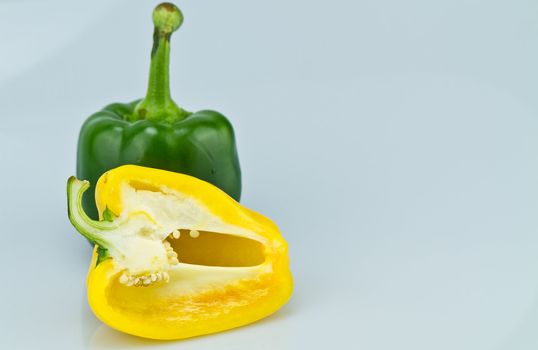 The green whole capsicum and cut yellow capsicum on bluish background