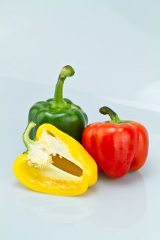 The green and red whole capsicums and a cut yellow capsicum on bluish background