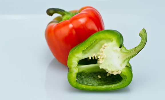 The red whole capsicum and cut green capsicum on bluish background