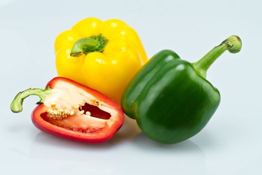 The green and Yellow whole capsicums and a cut red capsicum on bluish background