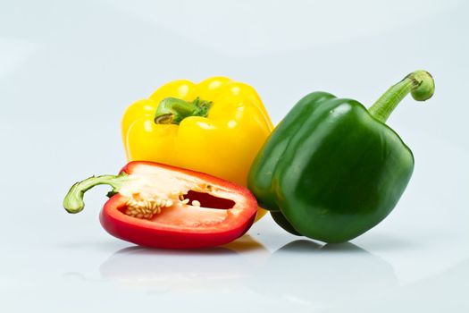 The green and Yellow whole capsicums and a cut red capsicum on bluish background