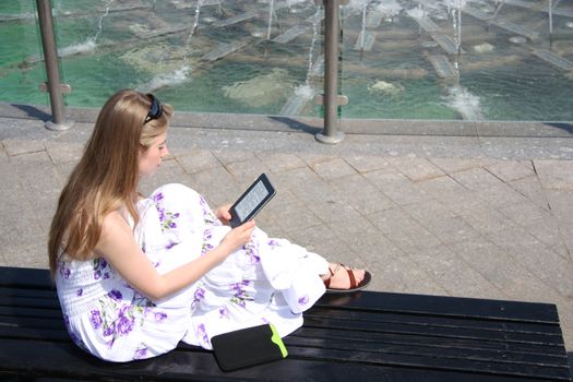 Young girl sitting on a bench and reading a digital book