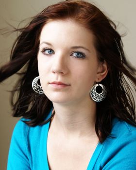 A young girl looks at the viewer with her big blue eyes and wind blown hair.