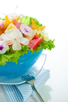 Fruit salad with edible flowers in a blue bowl from ice on white background