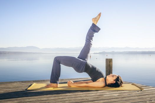 An image of a pretty woman doing yoga at the lake - Setu Bandha