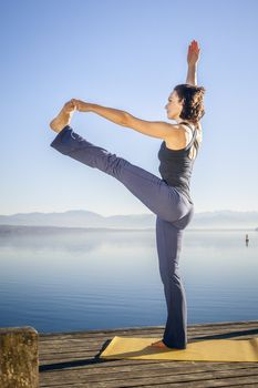 An image of a pretty woman doing yoga at the lake - Utthita Hasta Padangusthasana
