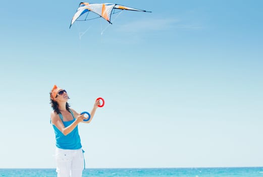 Young cute woman playing with a colorful kite on the tropical beach.