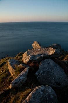 A pile of rocks on the coast in the red evening light and a view of the sea beyond.