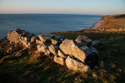 A stone wall in the red evening light and fields running down to the sea.