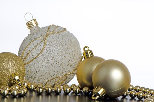 Golden christmas balls with decorations on black surface and white backdrop.
