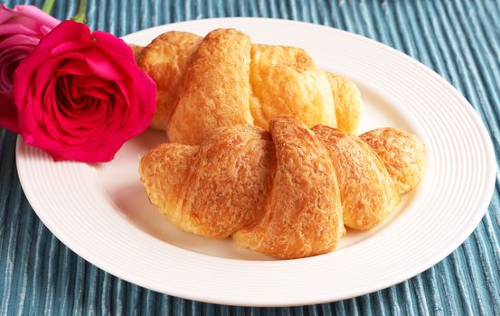 Breakfast plate with freshly baked croissants and pink roses on white plate