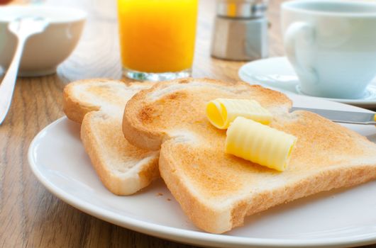 Breakfast table with butter on toast and a coffee cup in the background