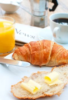 Breakfast spread with a buttered croissant, coffee and newspaper in the background