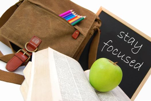 Satchel and books next to a blackboard with the words stay focused