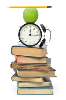 Balancing act of objects, including an apple and closk, on top of a stack of books 