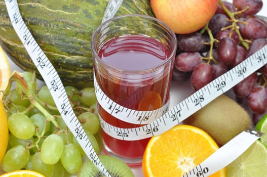 Various fruits around a glass of juice and a tape measure  