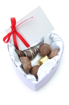 Assortment of chocolates inside a heartshaped box with a card and decorative red ribbon