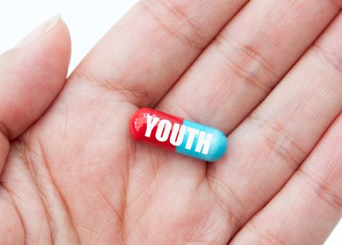 Hand holding a pill labelled with youth