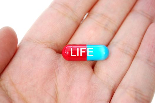 Hand holding a pill labelled with the word life  
