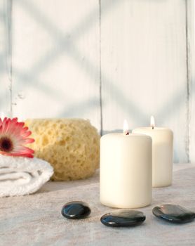 Spa setting with lit candles, zen stones and a natural sponge