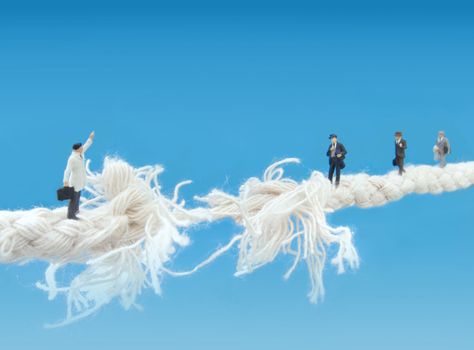 Miniature businessmen walking a breaking tightrope