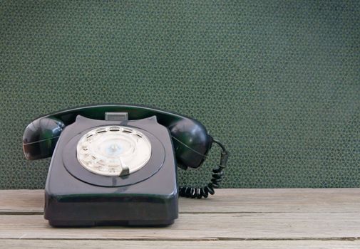 Vintage phone on a wooden table with wallpaper in the background