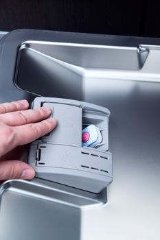 hand loads a dishwashing tablet into a dishwasher 