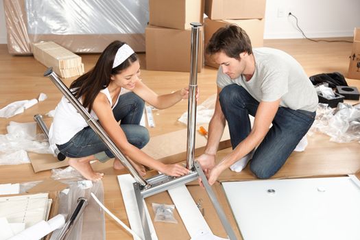 Couple moving in together assembling furniture table. Young interracial couple in new house or apartment home working together to assemble table. Asian woman, Caucasian man.
