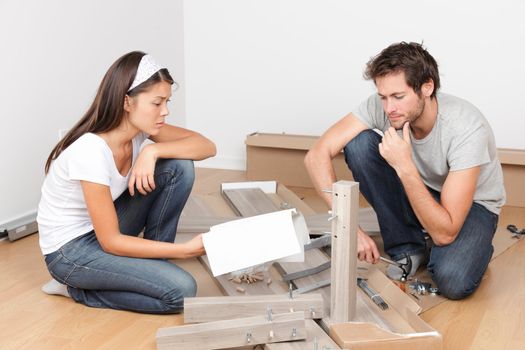 Couple moving in assembling bed furniture with problems and difficulties. Young interracial couple in new home. Asian woman, Caucasian man.