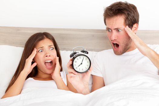 Oversleeping. Attractive young couple missed the ringing of the alarm clock and have overslept awakening and are late, reacting in horror at the time. Interracial couple, Asian woman, Caucasian man.