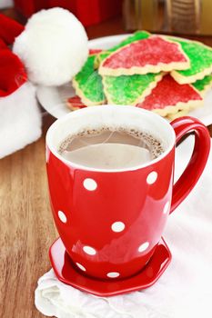 Cup of hot cocoa with Christmas cookies and Santas hat in the background. Shallow depth of field.
 
