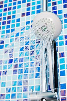 Shower head with running water against blue tiled bathroom wall