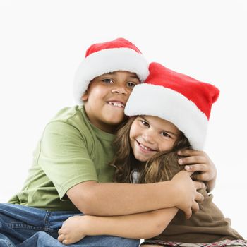 Hispanic brother and sister wearing santa hats hugging