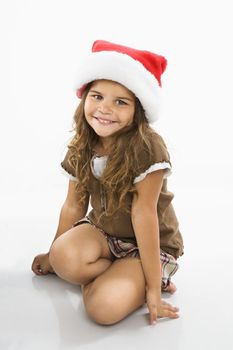 Little hispanic girl sitting on floor wearing santa hat.