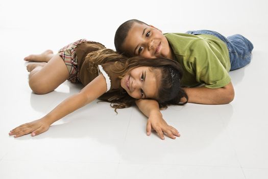 Portrait of Hispanic brother and sister lying on floor smiling at viewer.