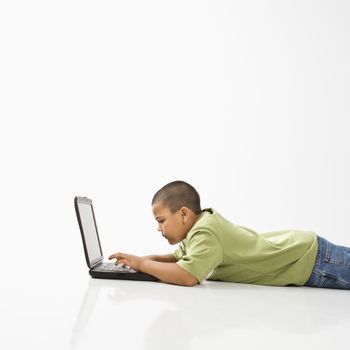 Young latino boy lying on floor using laptop computer.