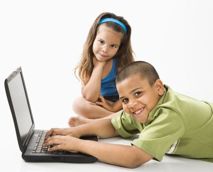 Young latino boy using laptop computer while girl watches.