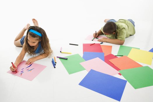 Young latino boy and girl coloring on construction paper and smiling.