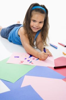 Young latino girl coloring on construction paper and smiling.