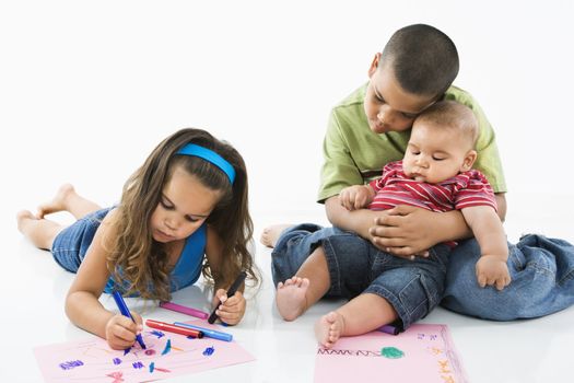 Young latino girl coloring on construction paper while brothers watch.