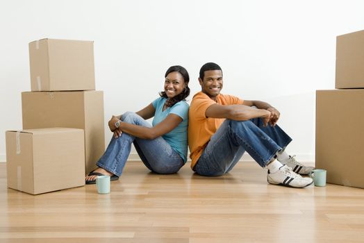 African American male and female couple sitting on floor next to moving boxes.