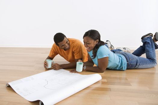 African American male and female couple lying on floor looking at architectural blueprints.