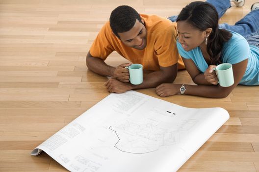 African American male and female couple lying on floor looking at architectural blueprints.