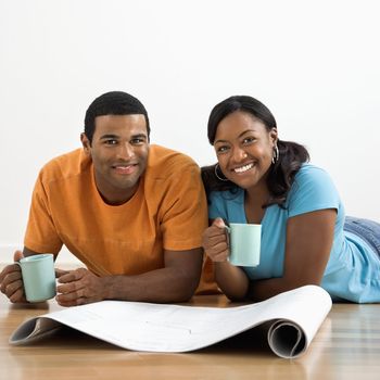 African American male and female couple with architectural blueprints drinking coffee.
