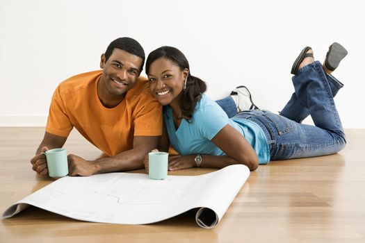 African American male and female couple with architectural blueprints drinking coffee.