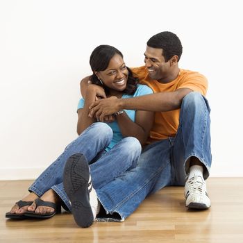 Happy, smiling African American couple sitting on floor snuggling.