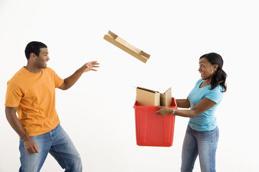 African American female holding recycling bin while male tosses cardboard into it.