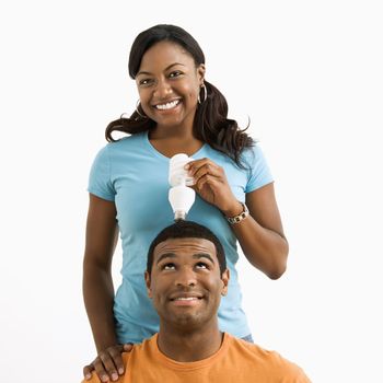 African American female holding energy-saving lightbulb over man's head.